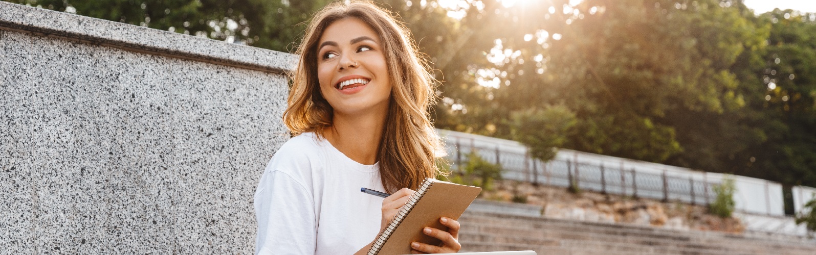 young brunette lady sitting cross legged near stairs with a laptop in her lap smiling