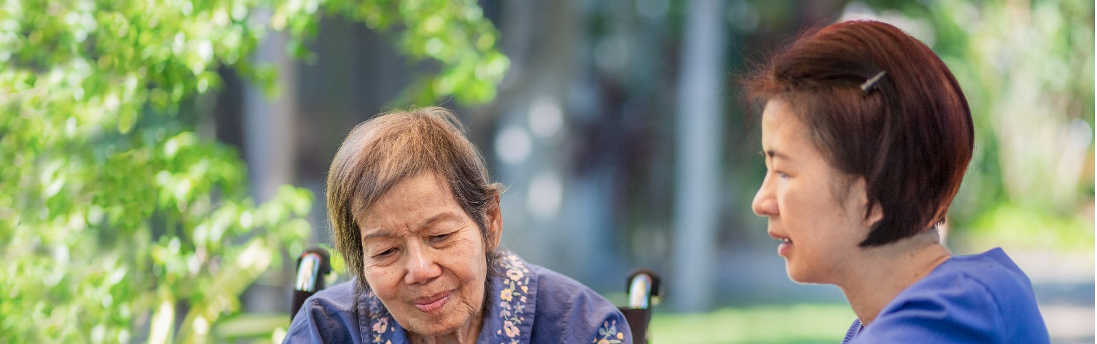 2 women working on a craft project together outside, one is in a wheelchair and one is in blue scrubs