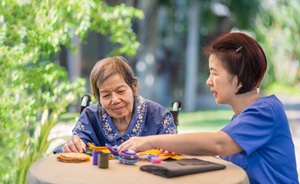 2 women working on a craft project together outside, one is in a wheelchair and one is in blue scrubs