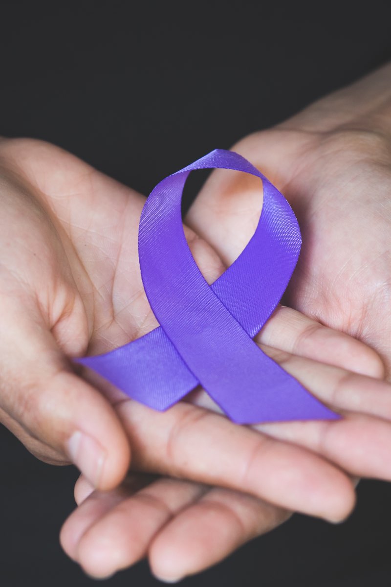 Two hands holding Domestic Violence Awareness Month purple ribbon