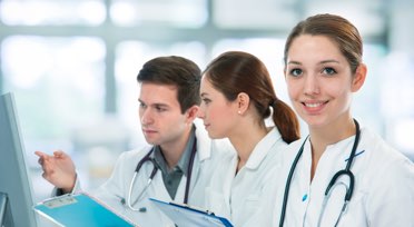 Female healthcare professional smiling while colleagues review information on computer