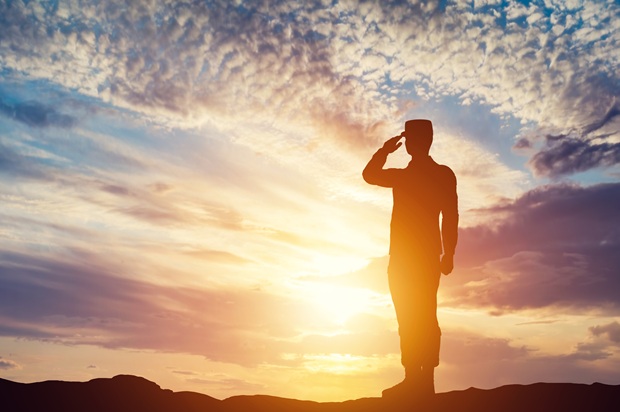 miilitary member in uniform saluting with a sunset behind them