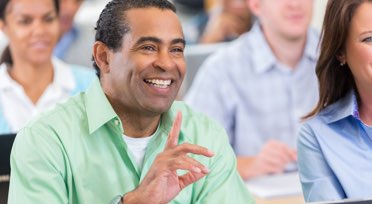 Male student in class raising hand and smiling