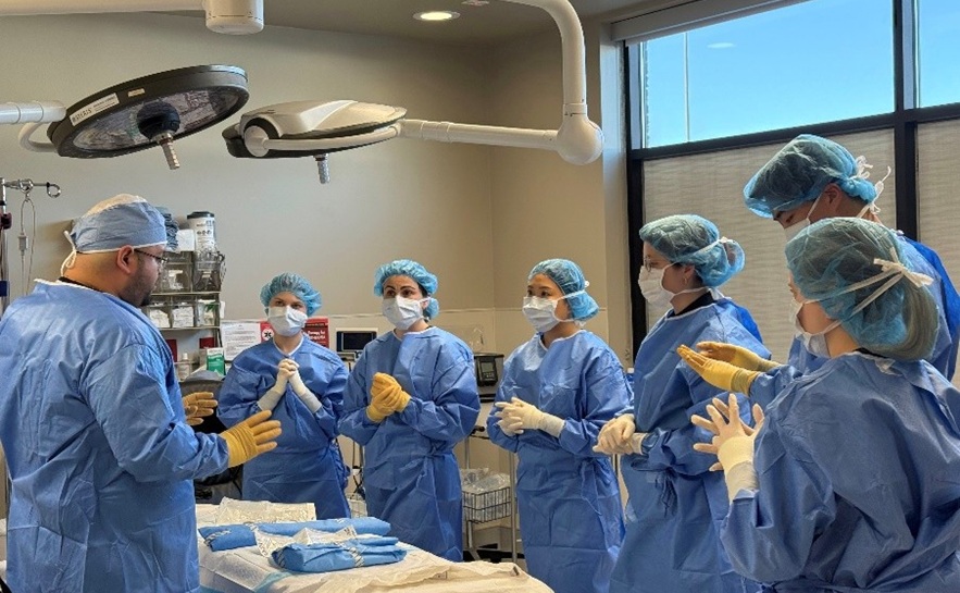 south students wearing surgical gowns getting instruction in a simulation operating room
