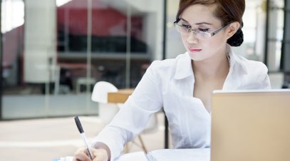 Female accountant at desk writing in front of laptop