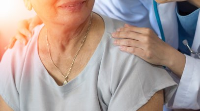 Nurse with hands on shoulders of older person smiling