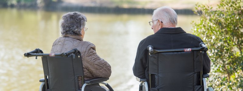 Older man and female in wheelchairs by lake