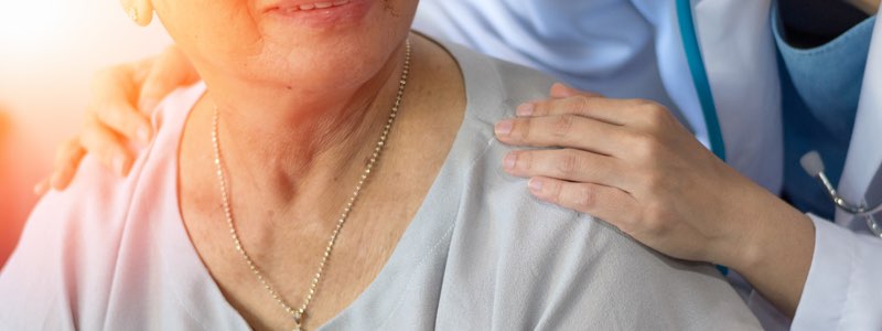 Nurse with hands on shoulders of older person smiling