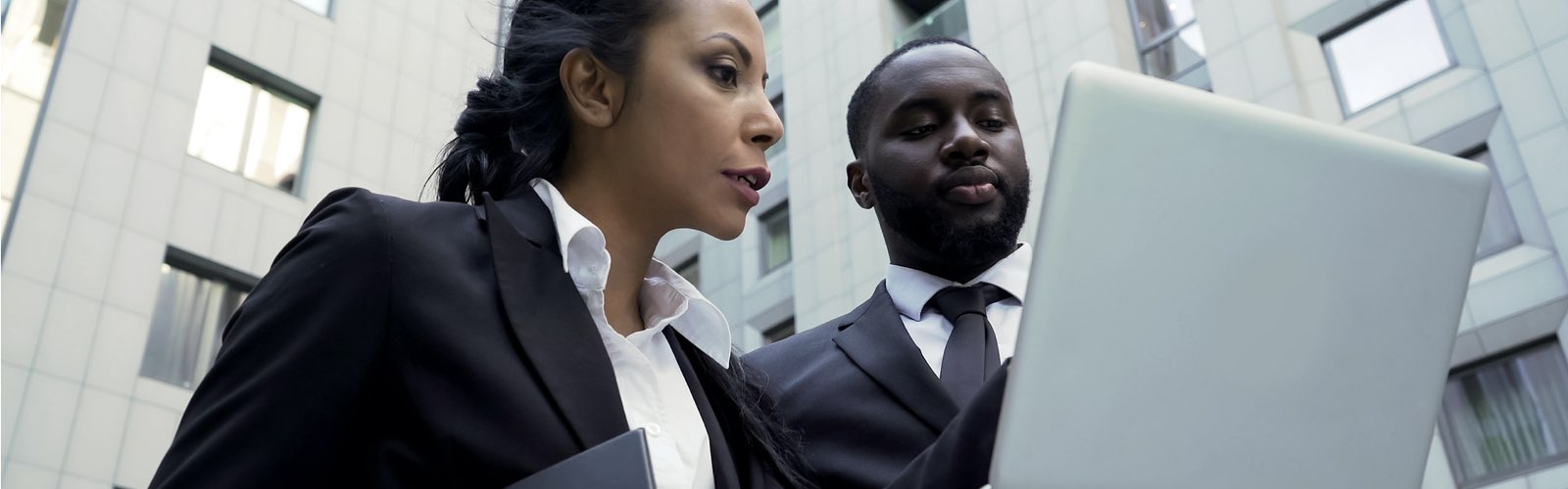 2 criminal justice professionals looking at laptop in front of office building