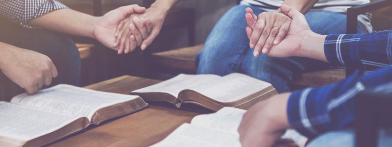 Group of people holding hands praying over bibles