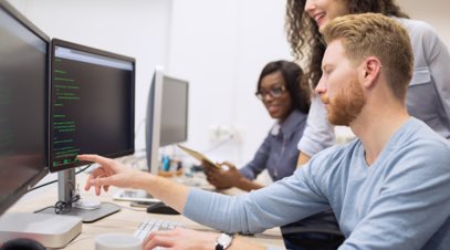 Information technology professional reviewing code on computer screen with team