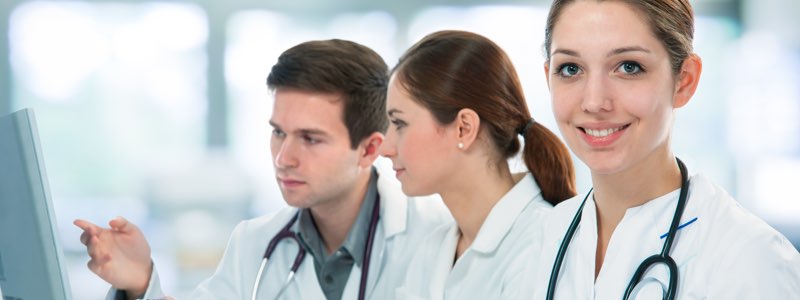 Female healthcare professional smiling while colleagues review information on computer