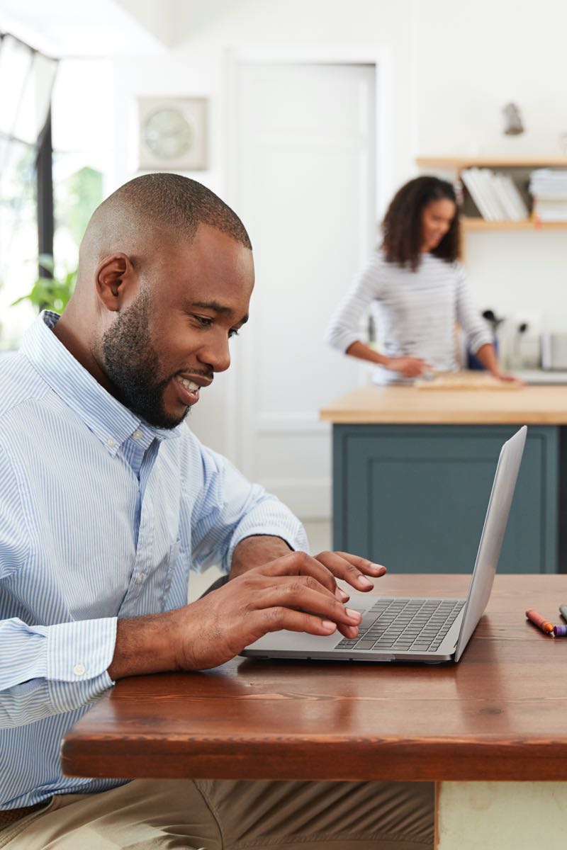 Male student at home with family learning on laptop