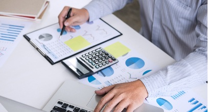 person in long sleeves typoing on a laptop while review charts on a desk