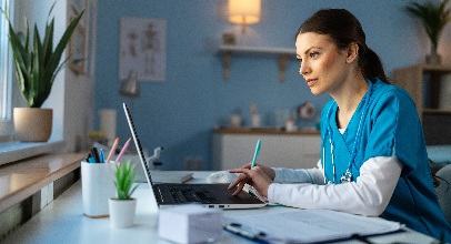 brown-haired healthcare personel in blue scrubs sitting at a desk studying the computer