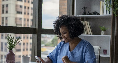 african american woman in scrubs sitting at a desk looking at her phone