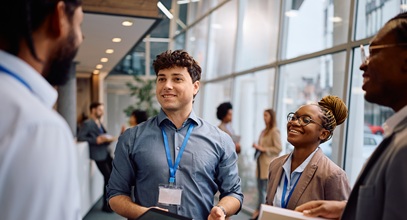 young man with curly brown hair and blue button-down shirts standing in a circle smiling at the other people