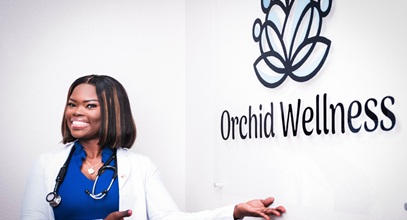 Chelsea Asanta in a white nursing coat and stethescope posing with the Orchid Wellness sign