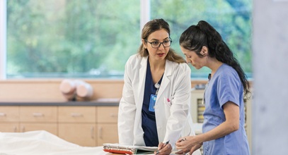 2 female healthcare workers in blue scrubs discussing information they are looking at on a clipboard