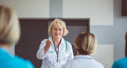blonde female health professional in her white coat at the front of a room teaching