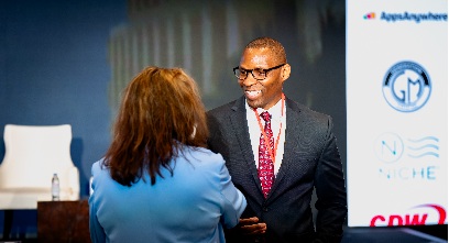 Dr. Gil Singletary, wearing a dark suit and red tie, shaking hands with a dark haired woman in a blue top