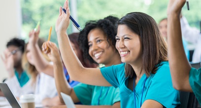 Nursing students in a classroom setting raising their hands
