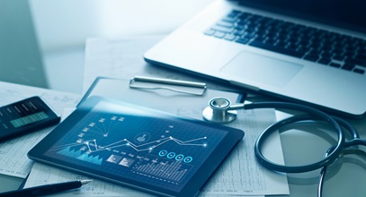 a tablet, a laptop, some papers, and a stethescope on a desk