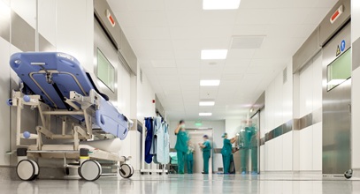 hospital hallway with a rolling hospital bed and severl staff in scrubs