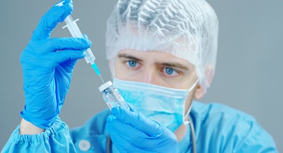 man in surgical scrubs, cap, and gloves holding a syringe and a bottle