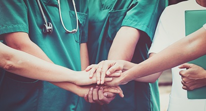 group of people in various colored scrubs stacking their hands on top of each other in a circle