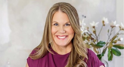 Nicole Early in a mauve dress with curled blonde hair and a flower in the background