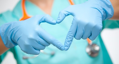 a person in blue scrubs making the heart symbol with both hands