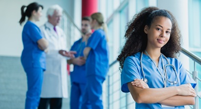 a nurse in blue scrubs standing in a hallway in front of a group of other healthcare workers in scrubs who are talking to each other