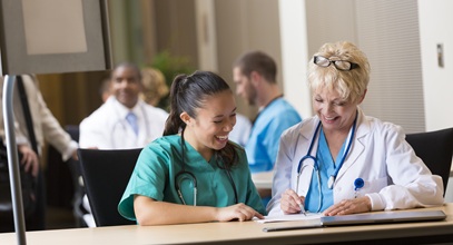 a female doctor and female nursing are looking at a notebook sitting at a long table