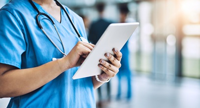 woman in blue scrubs looking at a table standing in a hallway
