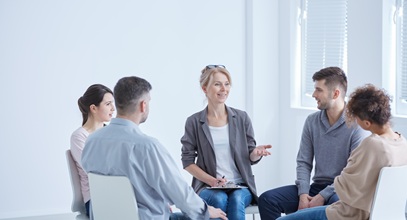 group of 5 people, three women and two men, sitting in a circle speaking with each other