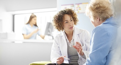 pharmacist in a white coat speaking with an older female patient in a blue coat in a hospital
