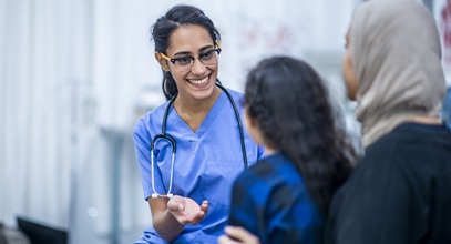 healthcare worker in blue scrubs and a stethoscope speaking to a child and her mother