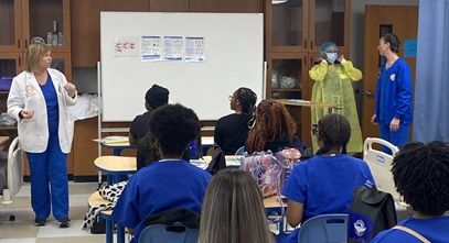 group of high school students in scrubs listening to a presentation by several healthcare professionals