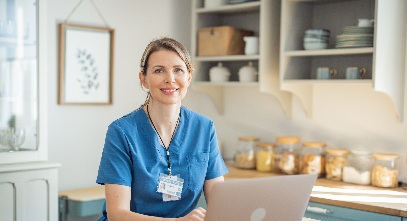 nurse in scrubs sitting at a desk in front of a laptop