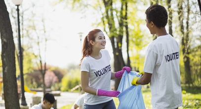 two young men and one woman picking up trash in a park wearing white tshirts that say volunteer