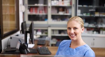 blonde woman in scrubs sitting in front of a computer in a hospital office