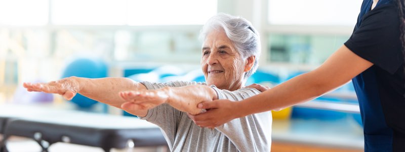 Occupational therapist holding older patient's arms outstretched